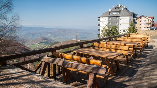 A wooden deck with benches overlooking a mountainous landscape and a building with a sloped roof. - JollyKop (Raška)