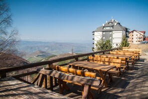 A wooden deck with benches overlooking a mountainous landscape and a building with a sloped roof. - JollyKop (Raška)