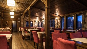 A rustic wooden interior with tables and chairs, stone walls, and a view of the outdoors. - JollyKop (Raška)