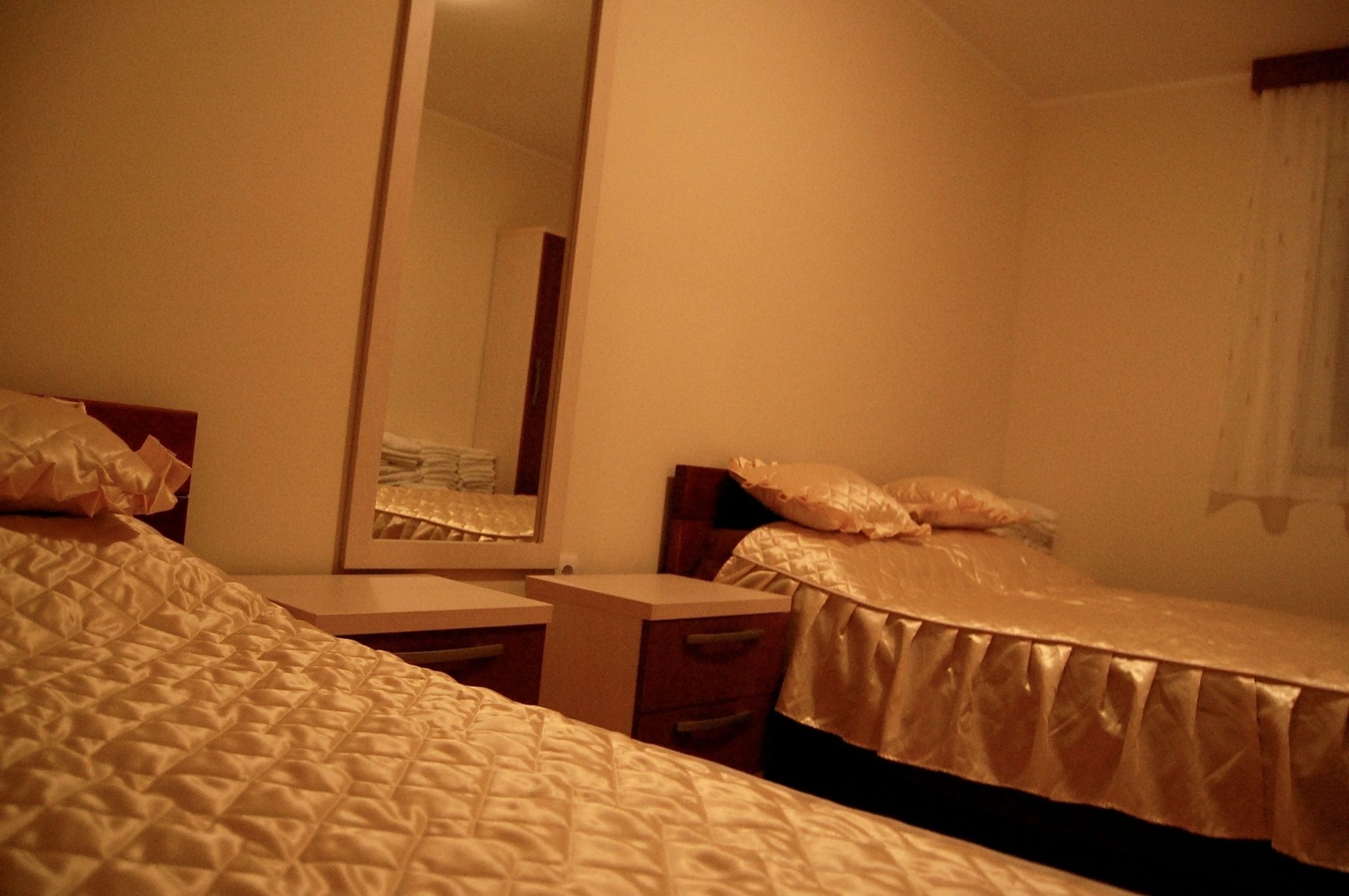 A hotel room with two beds, a bedside table, a mirror, and a window with curtains.