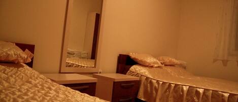 A hotel room with two beds, a bedside table, a mirror, and a window with curtains.