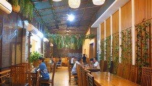 A restaurant with wooden tables and chairs, hanging plants, and pendant lights. - Puri Denpasar Hotel (Jakarta)