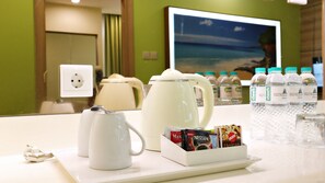 A hotel room counter with a coffee maker, tea kettle, and a beverage dispenser.