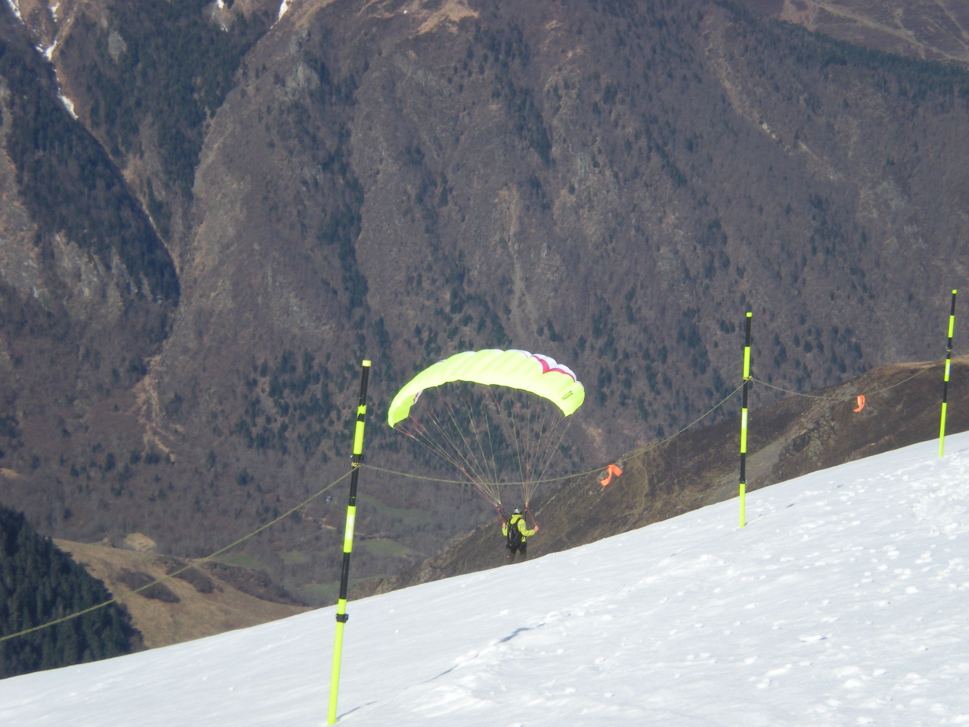 Una persona practicando parapente sobre un paisaje nevado con montañas al fondo.
