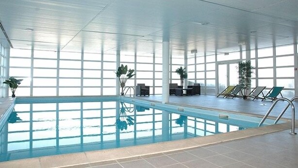 An indoor swimming pool with clear glass walls, lounge chairs, and potted plants. - Les Adrets de Peyragudes (Germ)