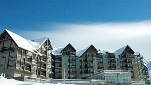 A multi-story hotel with a modern architectural design, featuring balconies and a snow-covered landscape with mountains in the background. - Les Adrets de Peyragudes (Germ)
