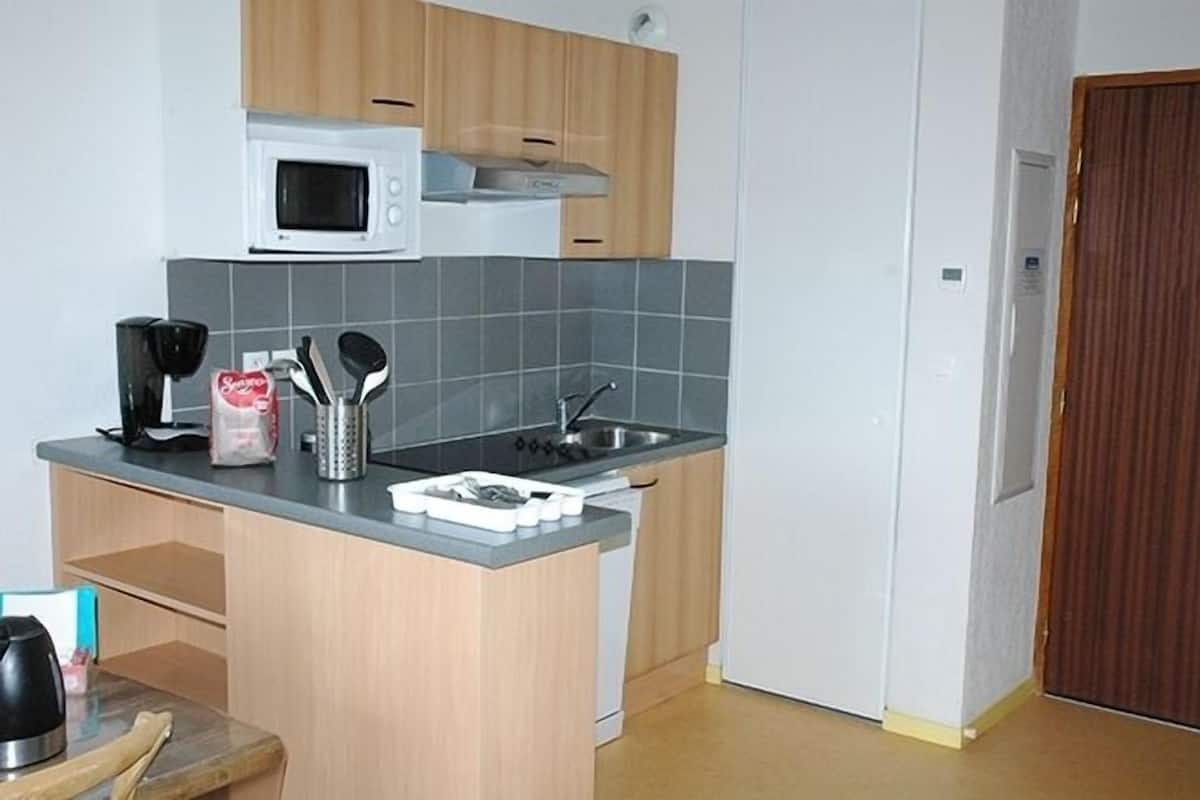 Een kleine keuken met een magnetron, spoelbak en basiskookgerei.