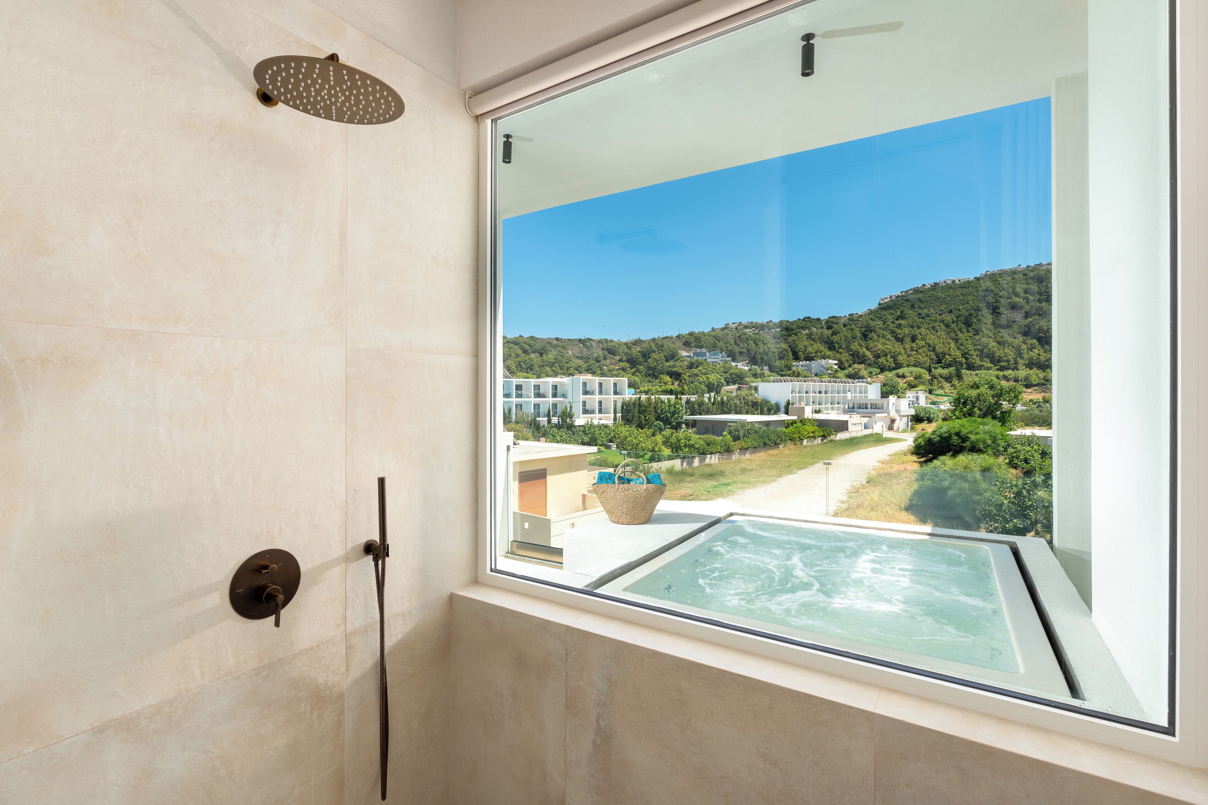 A modern bathroom with a large window, a glass shower enclosure, and a view of a residential area with houses and greenery.