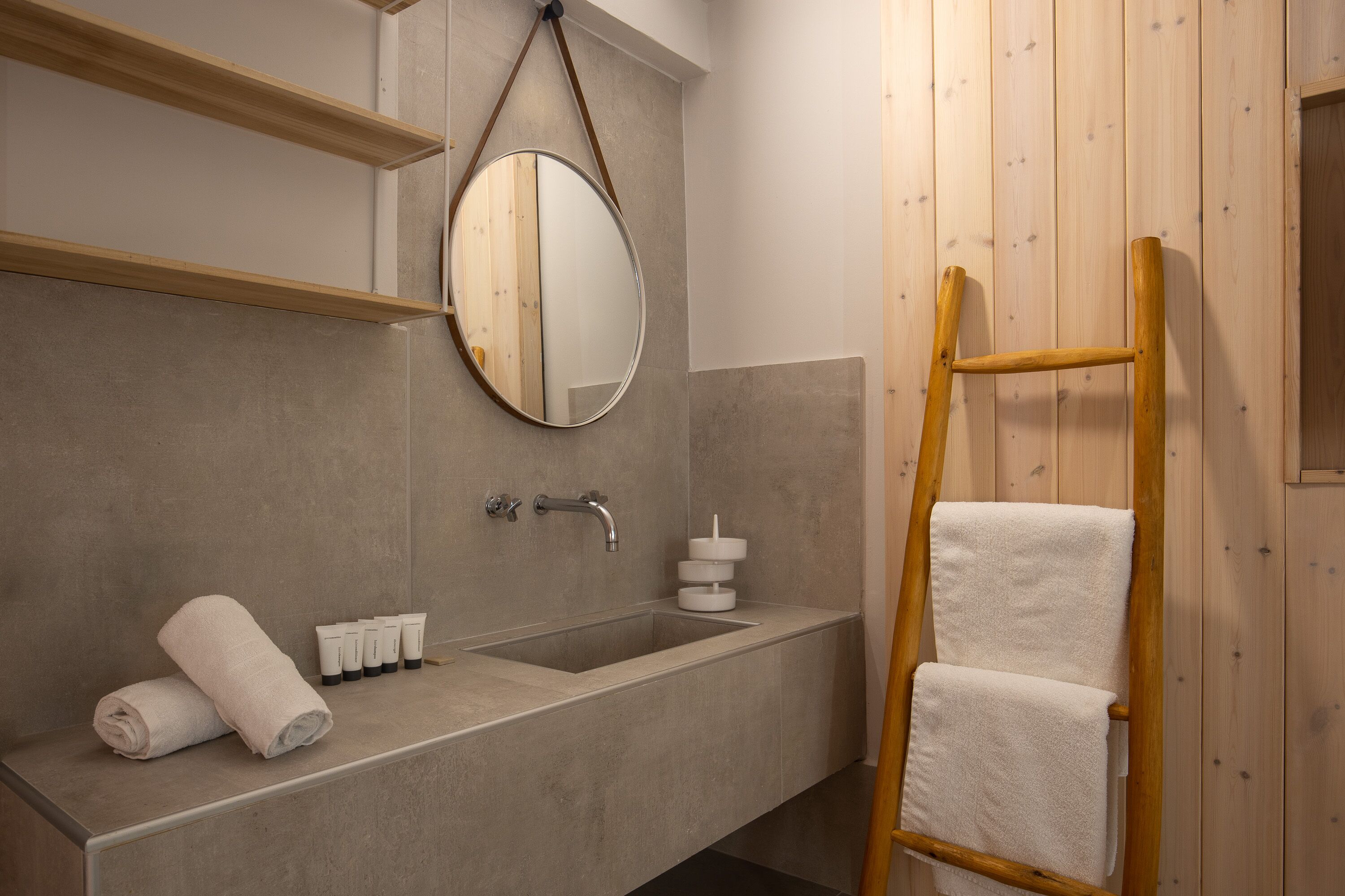 A bathroom with a wooden ladder, a large mirror, a sink, and neatly folded towels.