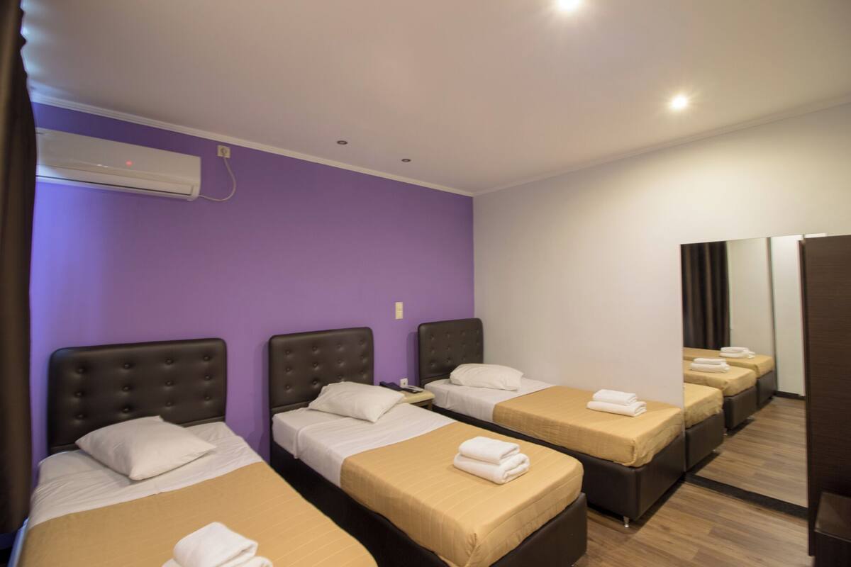 Habitación de hotel con tres camas individuales, cada una con cabecera y mesita de noche.