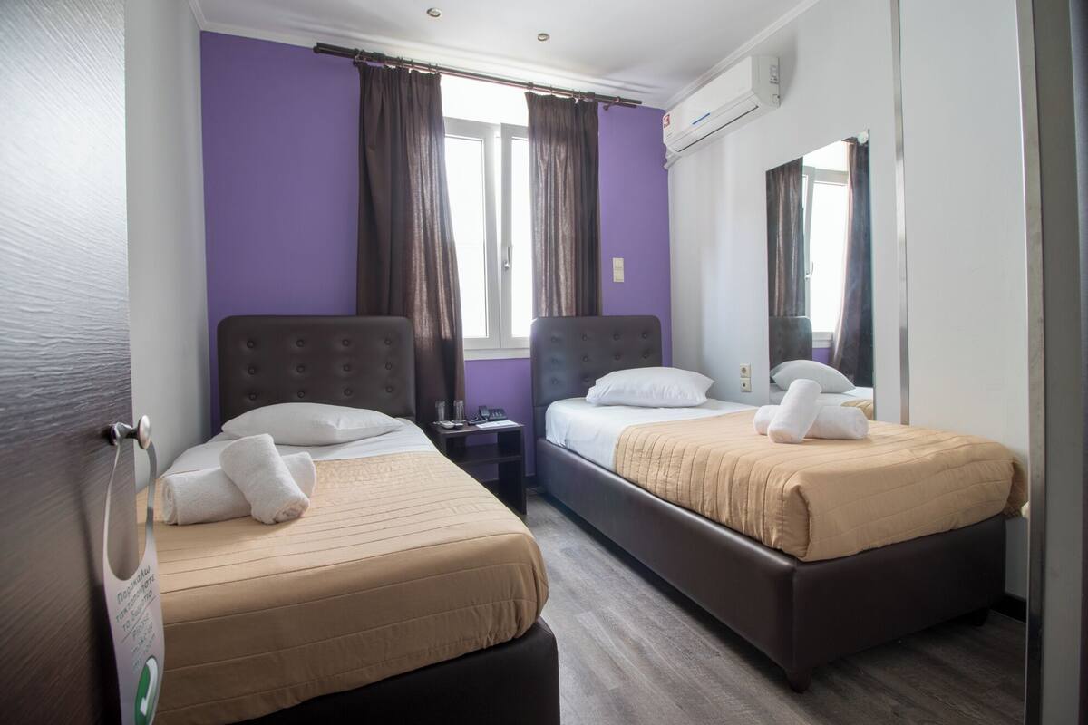 Habitación de hotel con dos camas, paredes moradas y un espejo grande.