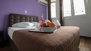 Une chambre d’hôtel avec un lit, un panier de fruits, une bouteille de vin et une fenêtre avec des rideaux.