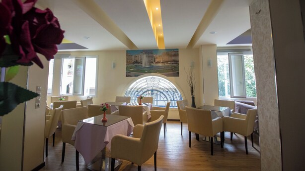 Un espace repas avec des tables et des chaises rondes, une grande fenêtre en arc de cercle et un tableau représentant un paysage urbain accroché au mur.