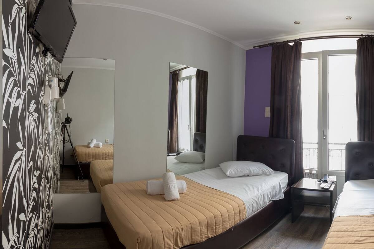 Habitación de hotel con dos camas, un espejo, una ventana con cortinas, un equipo de aire acondicionado y una pequeña mesa.