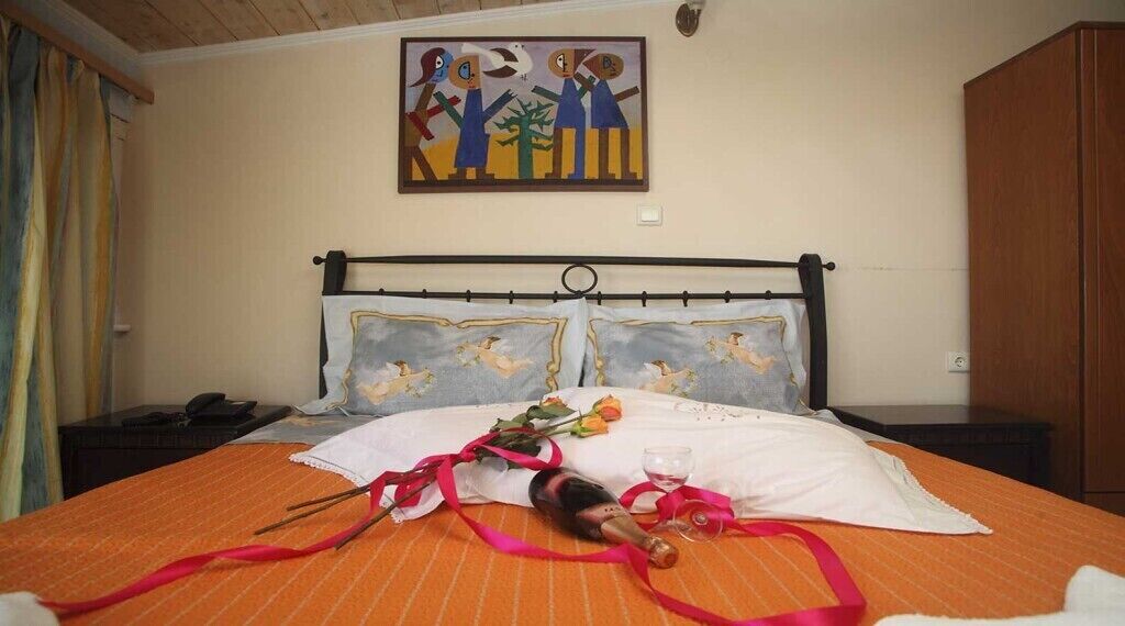 Una cama con una colcha blanca y naranja, una botella de champán y un ramo de flores.