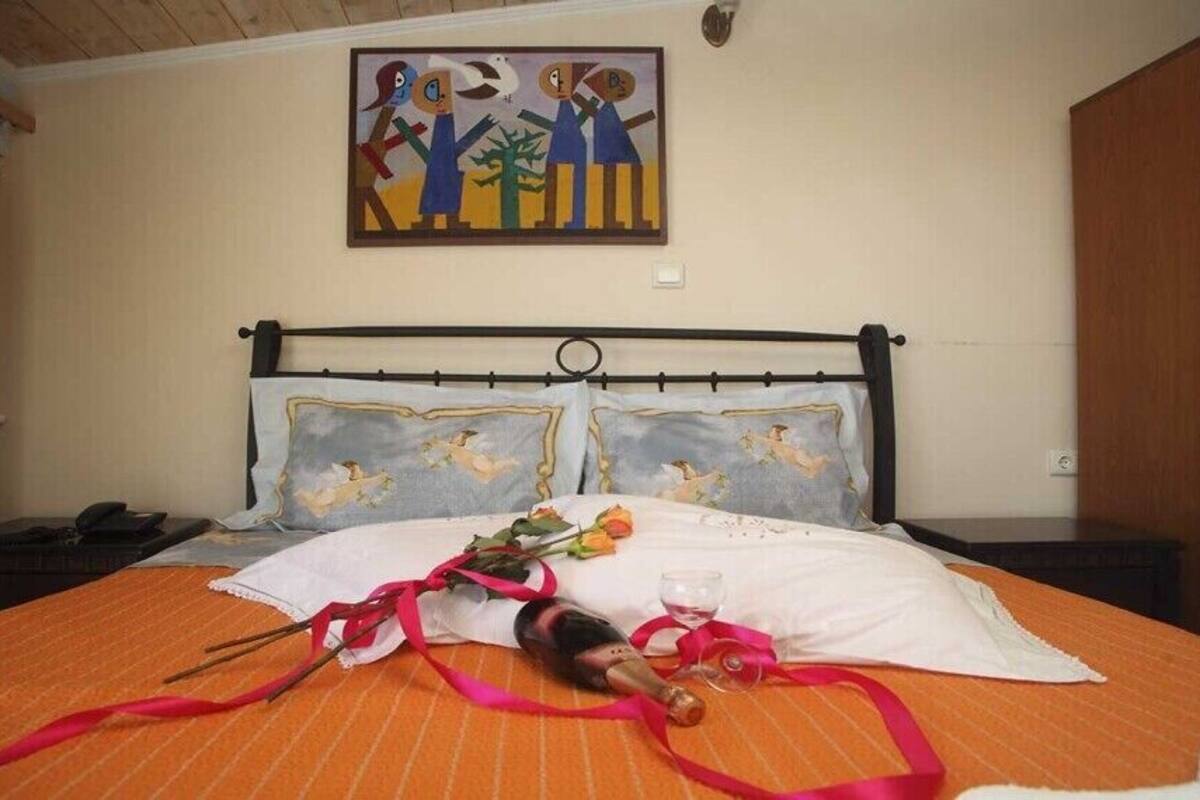 Ein Bett mit weiß-orange gestreifter Bettdecke, eine Champagnerflasche und ein Blumenstrauß.