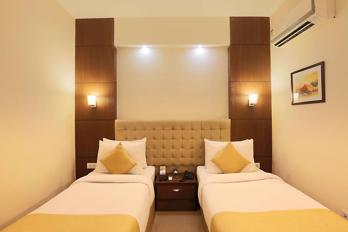 A hotel room with two beds, a wooden headboard, bedside lamps, a nightstand, and an air conditioning unit.