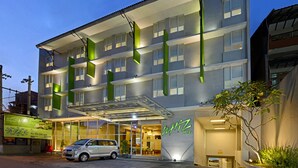 A modern hotel with a glass entrance, multiple floors, and green signage. - Whiz Hotel Malioboro Yogyakarta (Yogyakarta)