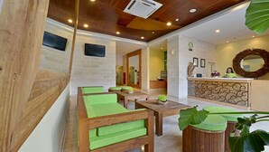 A reception area with a wooden reception desk, green cushioned seating, and a large mirror. - Whiz Hotel Malioboro Yogyakarta (Yogyakarta)