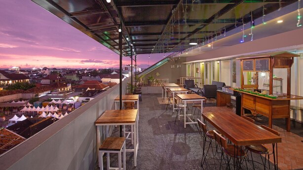 A rooftop terrace with tables and chairs, a coffee station, and a city view at sunset. - Whiz Hotel Malioboro Yogyakarta (Yogyakarta)