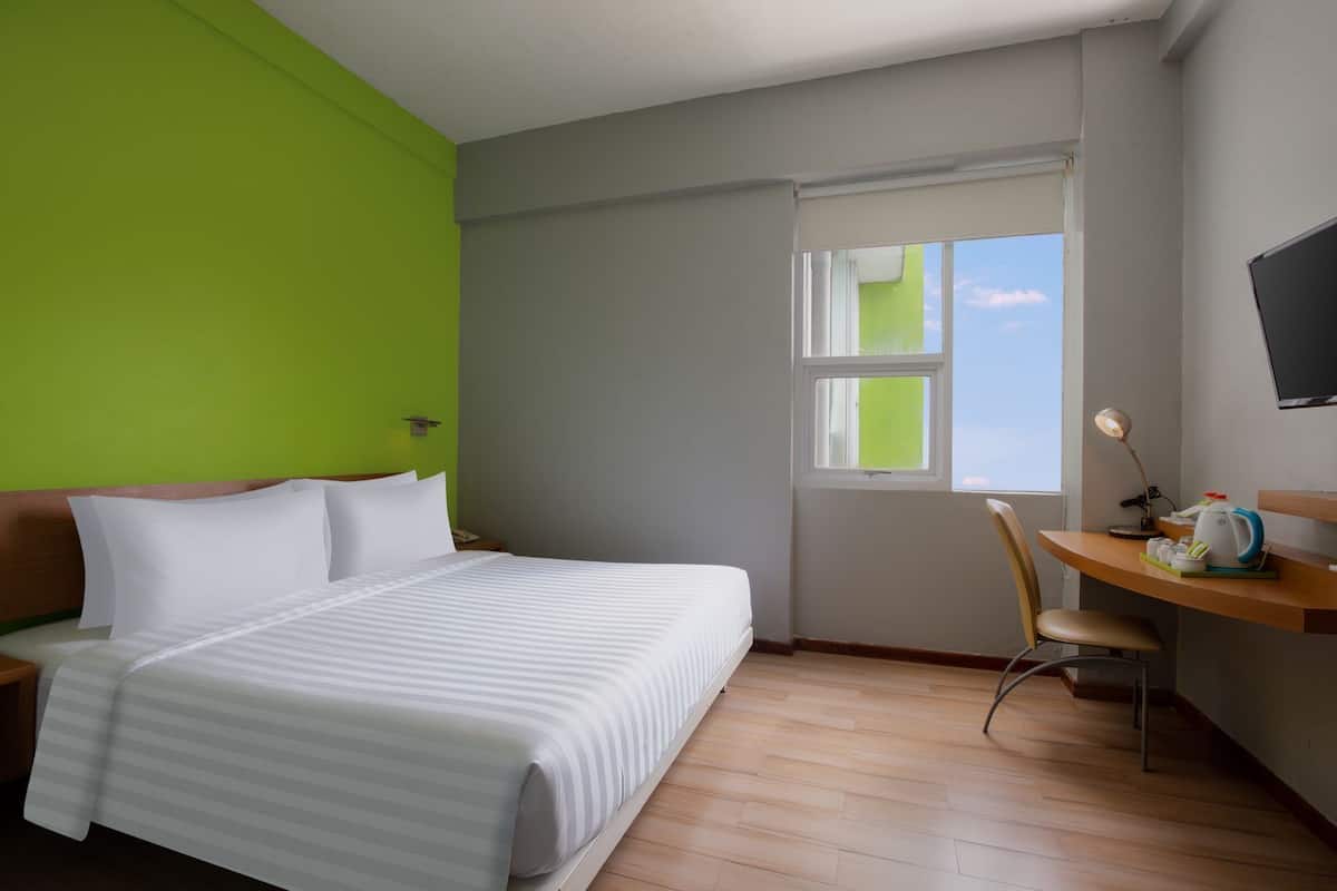 Ein Hotelzimmer mit einem Bett, einem Schreibtisch, einem Sessel, einem Fenster und einem Fernseher an der Wand.