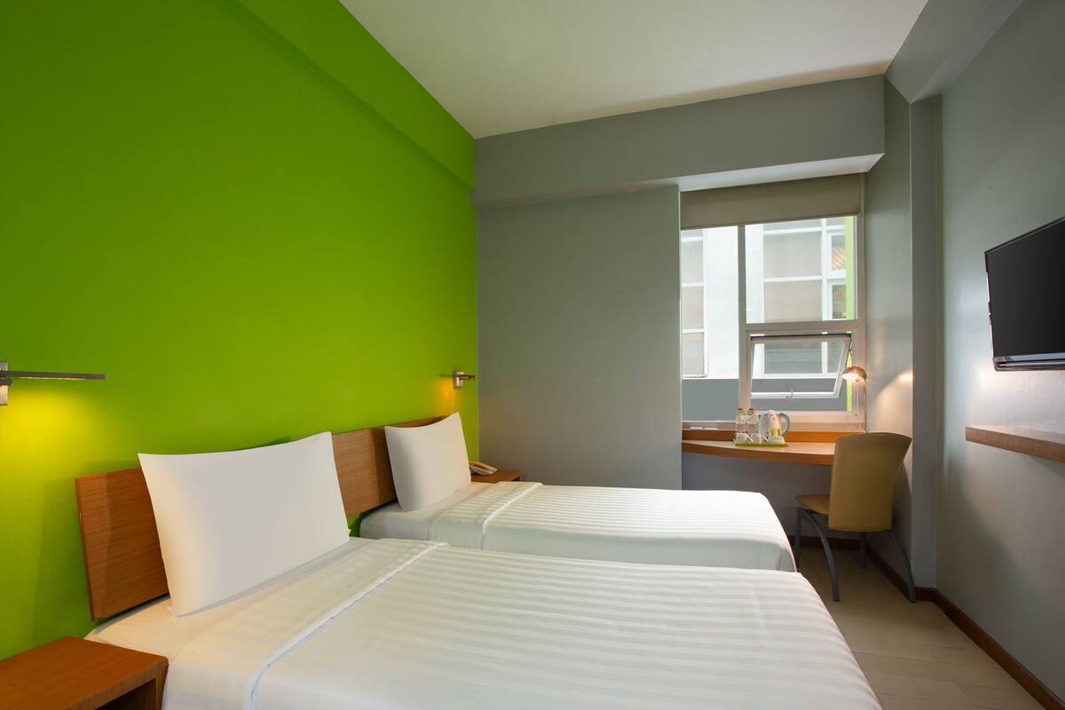 Ein Hotelzimmer mit zwei Betten, einem Schreibtisch, einem Stuhl, einem Fernseher und einem Fenster mit Blick.