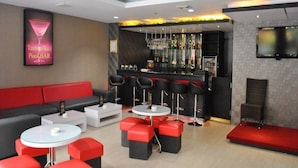 Ein moderner Loungebereich mit Bar, Sitzgelegenheiten in Rot und Schwarz sowie einem Fernsehbildschirm.