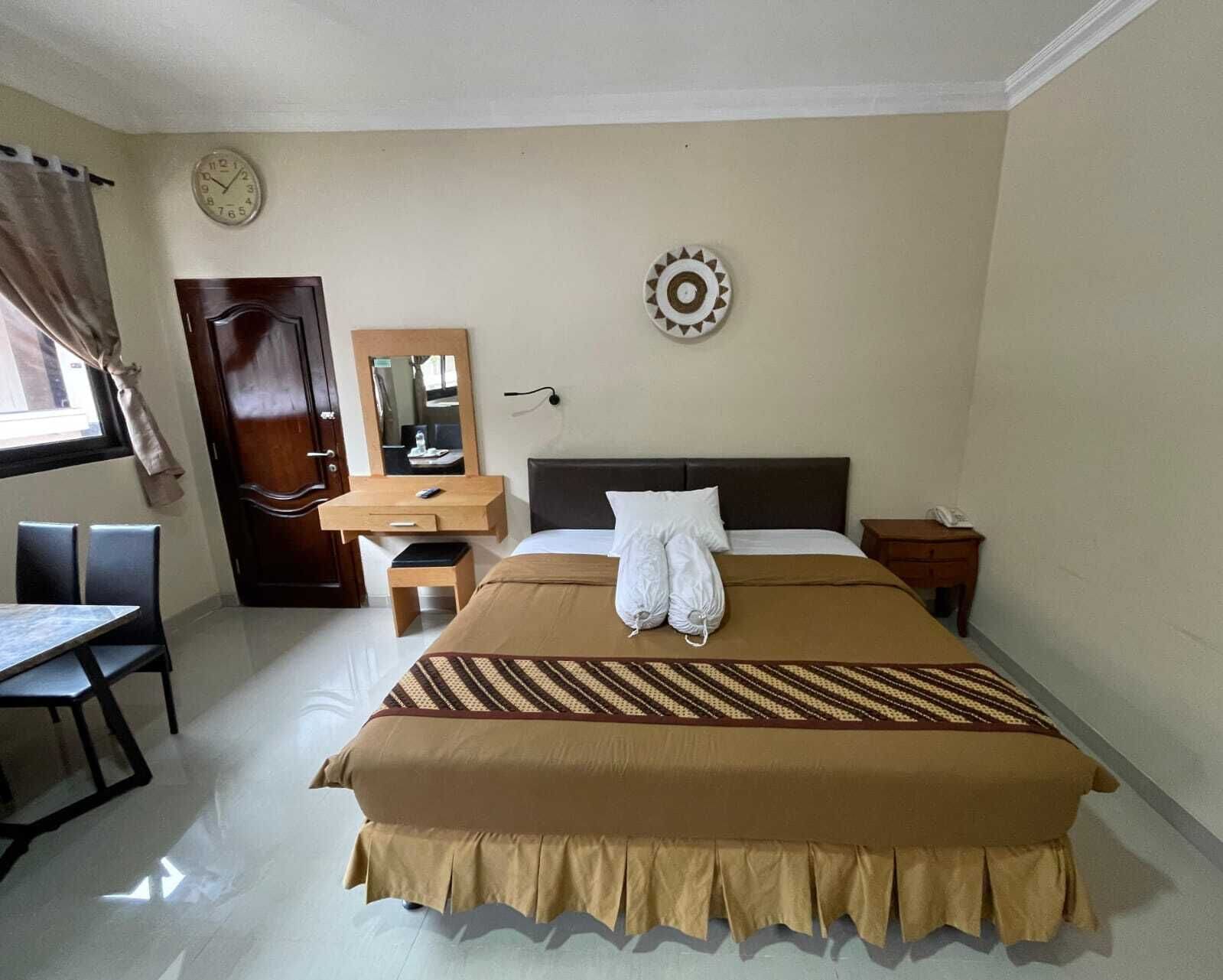 A hotel room with a bed, a desk, a chair, a clock, and a mirror.