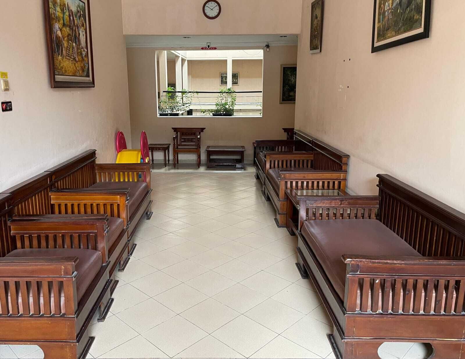 A church interior with wooden pews arranged in rows, a clock on the wall, and a view of a balcony with plants.