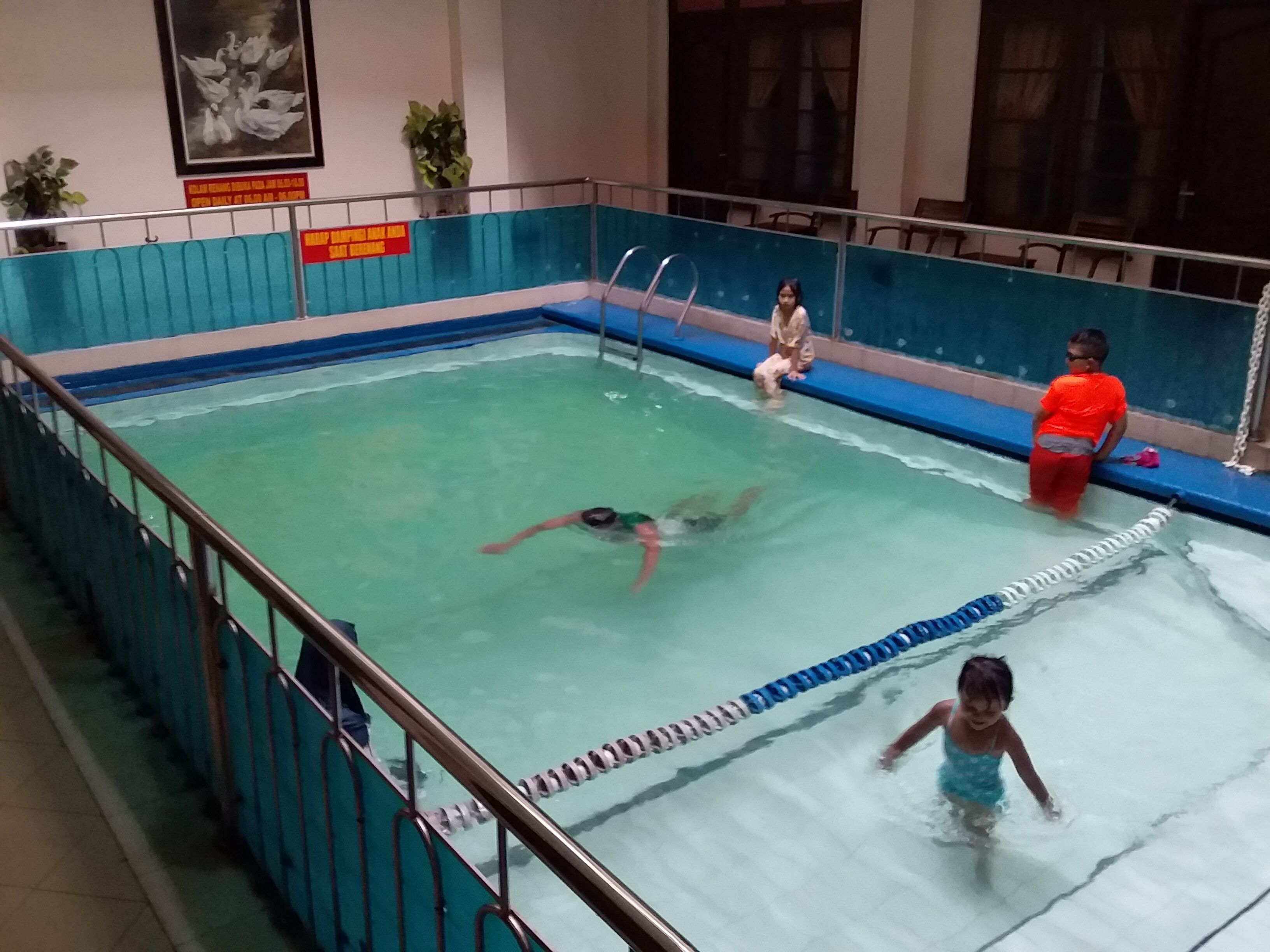 An indoor swimming pool with clear lanes, a diving board, and a safety sign on the wall.
