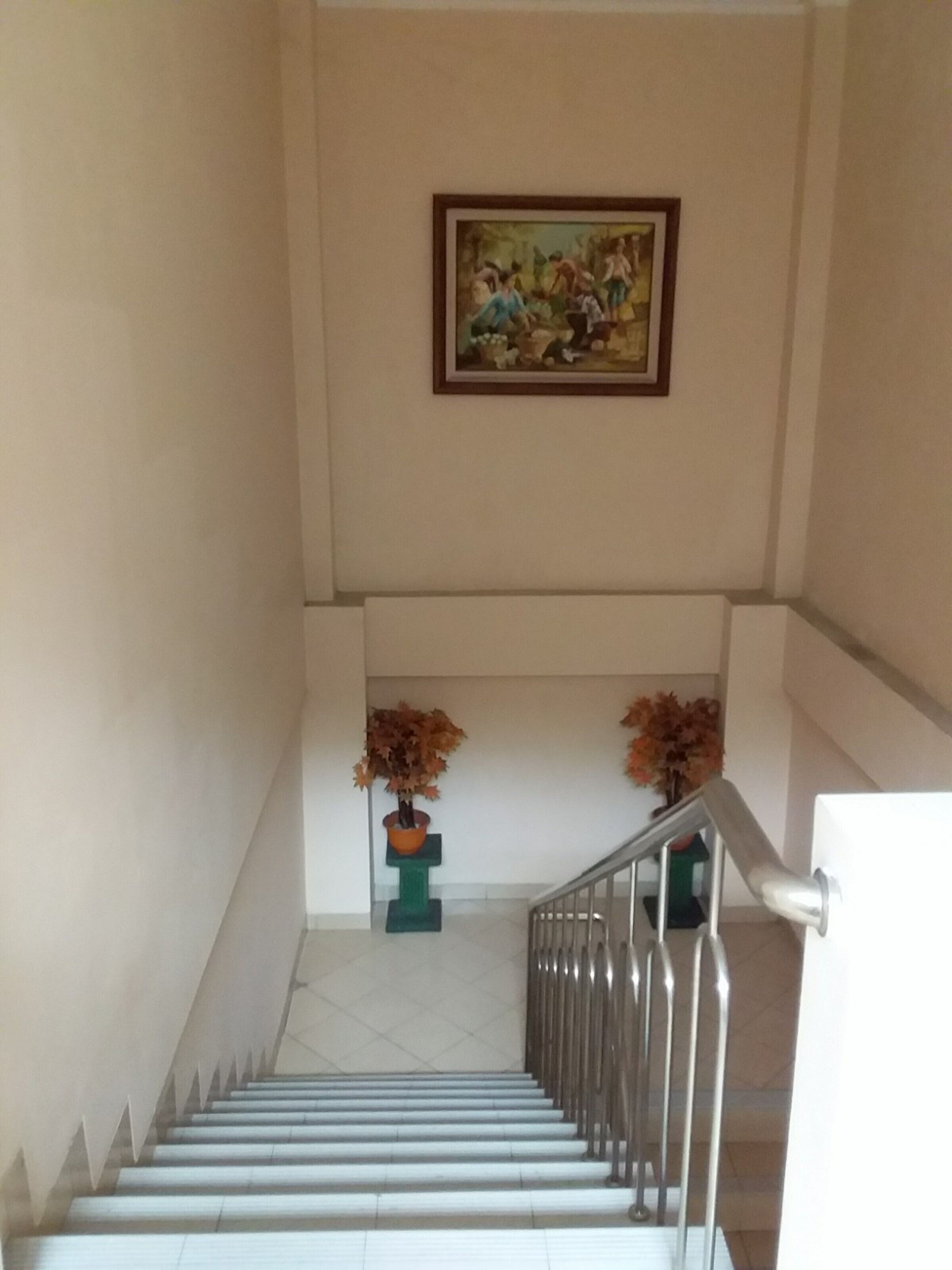 A staircase with a metal railing, a framed painting on the wall, and two potted plants at the bottom.