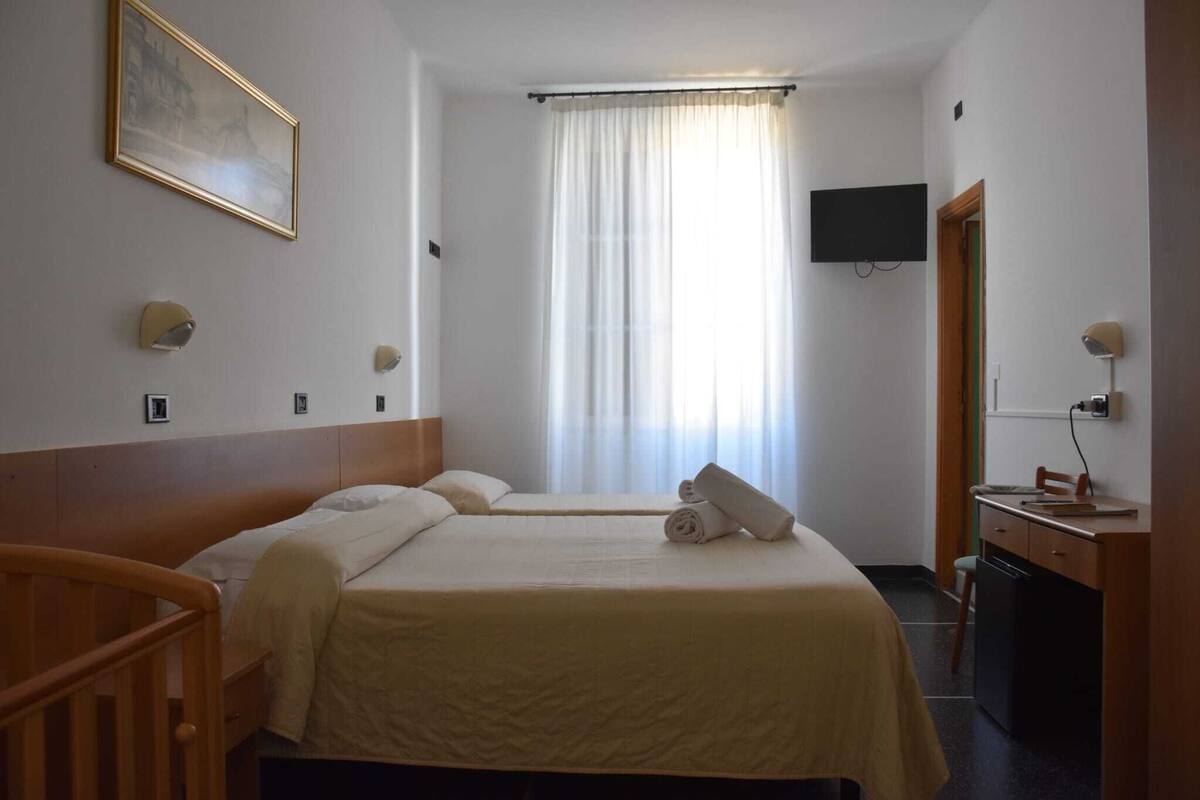 Une chambre d’hôtel avec deux lits, un bureau, une chaise, une télévision et une fenêtre avec des rideaux.