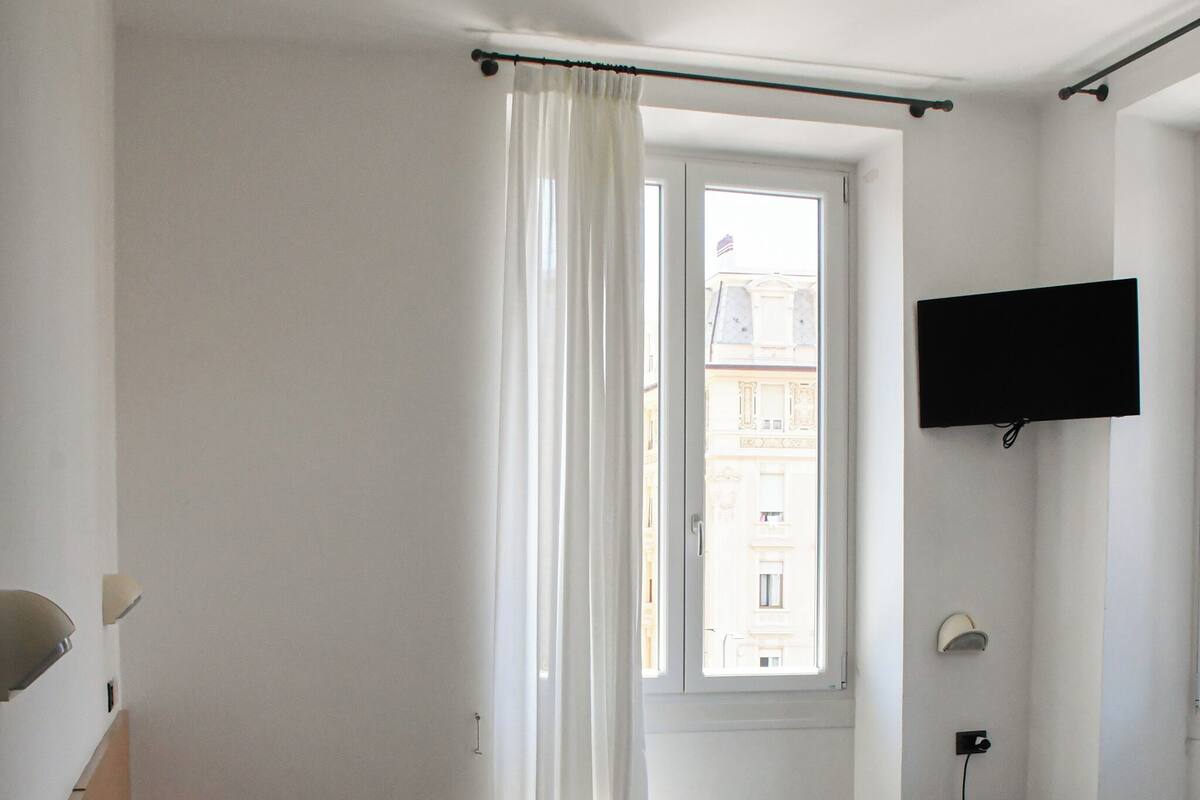 Une chambre d’hôtel avec un lit, un bureau, un téléviseur fixé au mur et une fenêtre avec des rideaux.
