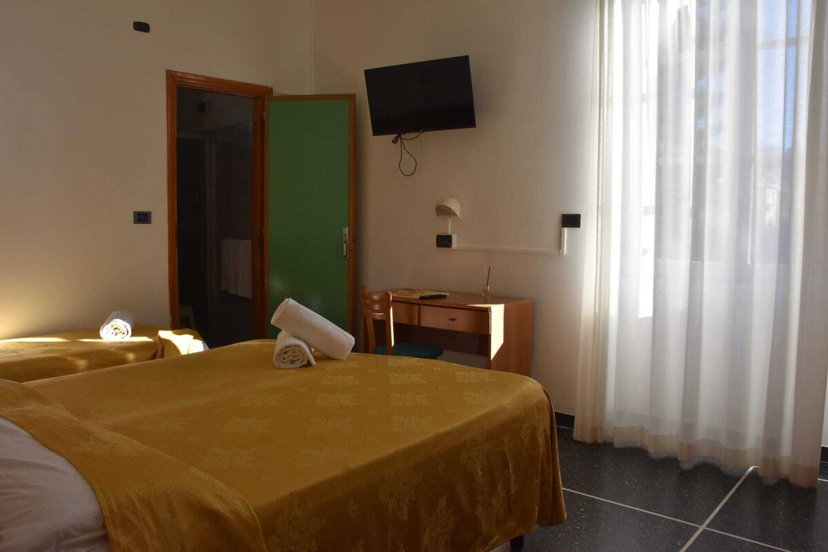 Une chambre d’hôtel avec deux lits, un bureau, une chaise, une télévision et une fenêtre avec des rideaux.