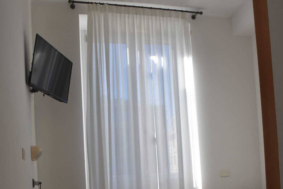 Une chambre d’hôtel avec un lit, un bureau doté d’un téléviseur à écran plat et une fenêtre ornée de rideaux légers.