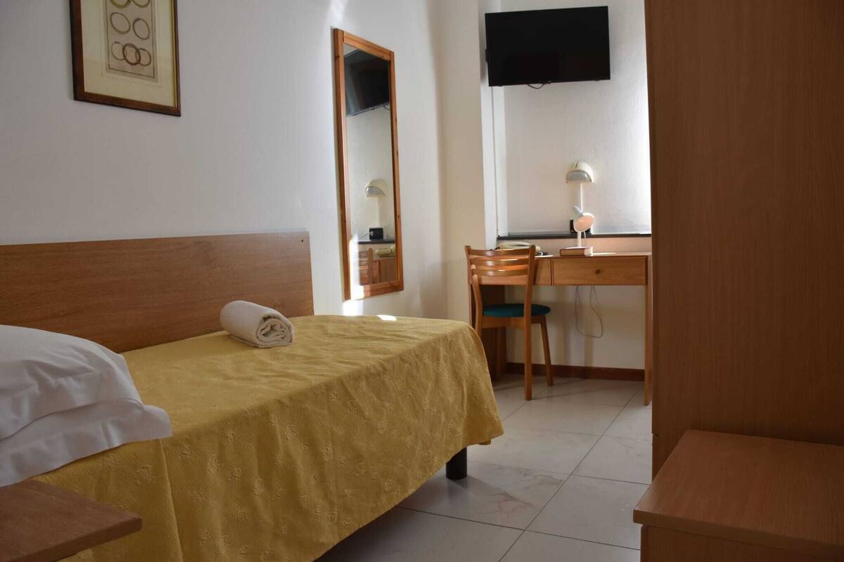 Une chambre d’hôtel avec un lit, un bureau, une chaise, un téléviseur fixé au mur et un tableau encadré accroché au mur.