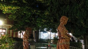 Un espacio exterior nocturno con dos estatuas, una piscina pequeña y una valla.