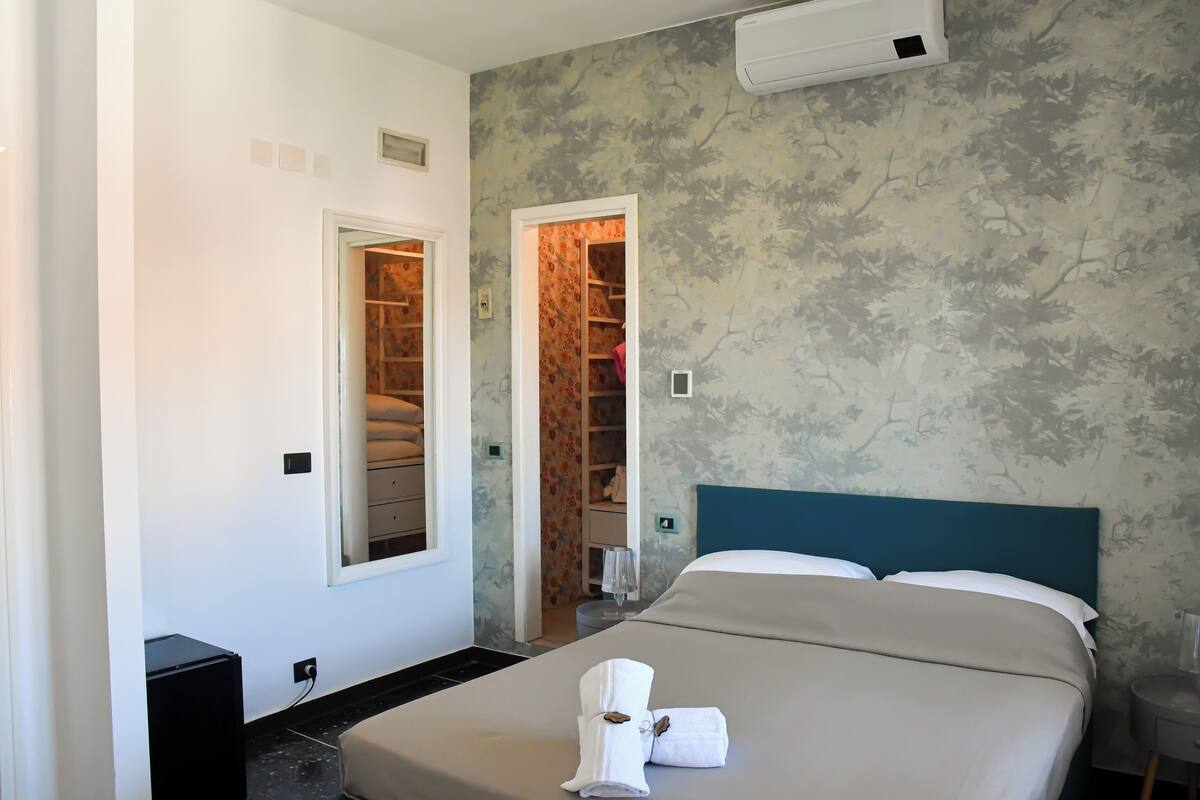 Une chambre d’hôtel avec un lit, une armoire, un miroir et une petite table avec un verre.