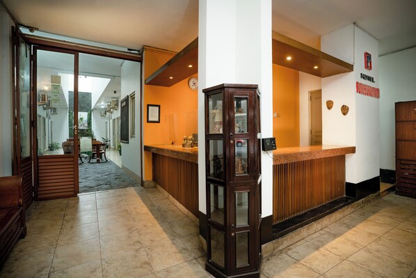 Zona de recepción de un hotel con un mostrador de madera, un reloj en la pared y un cartel con el nombre del hotel.