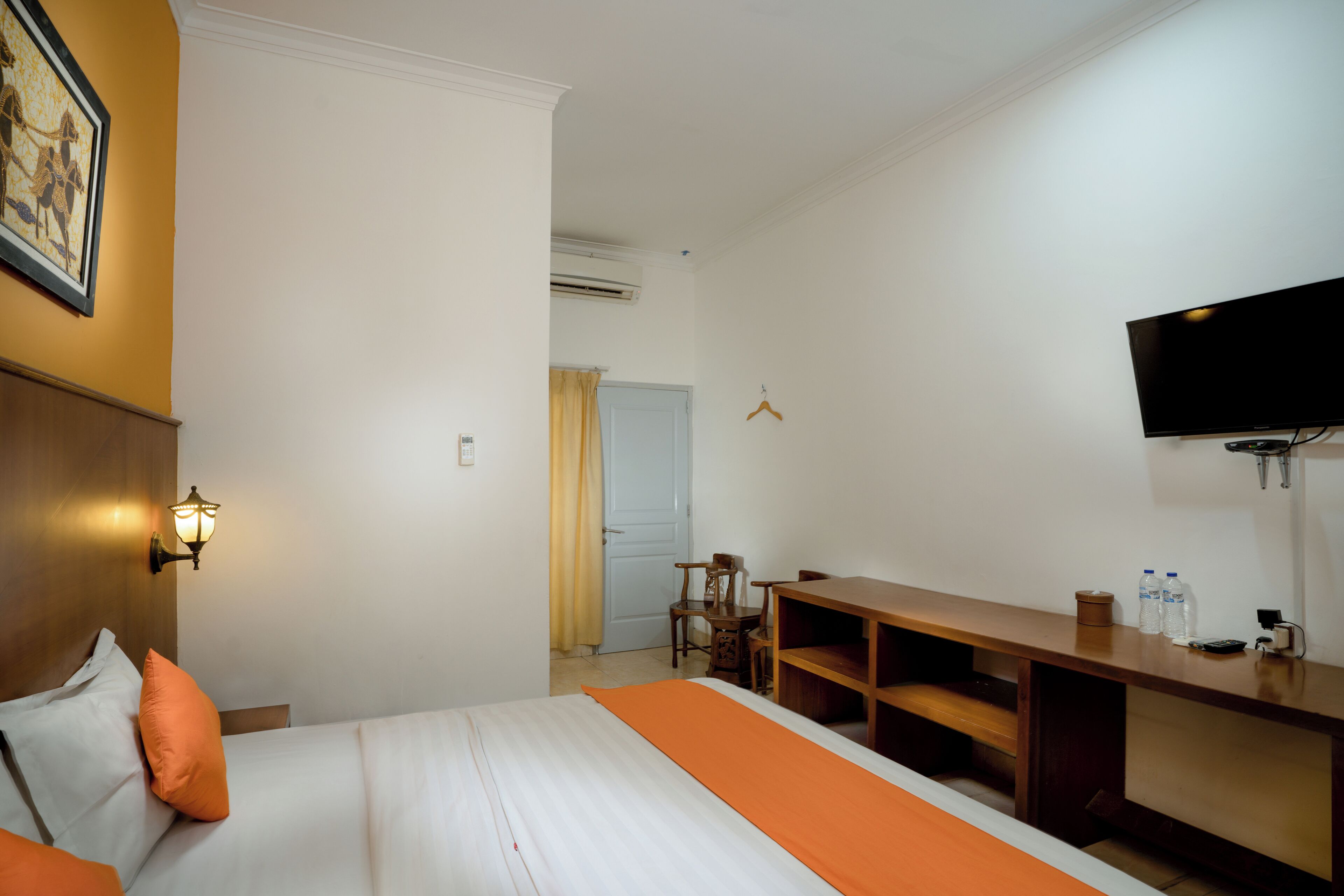 Habitación de hotel con cama, escritorio, silla, televisión y lámpara fijada a la pared.