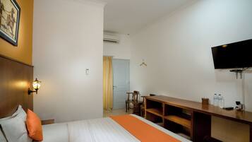 Habitación de hotel con cama, escritorio, silla, televisión y lámpara fijada a la pared.