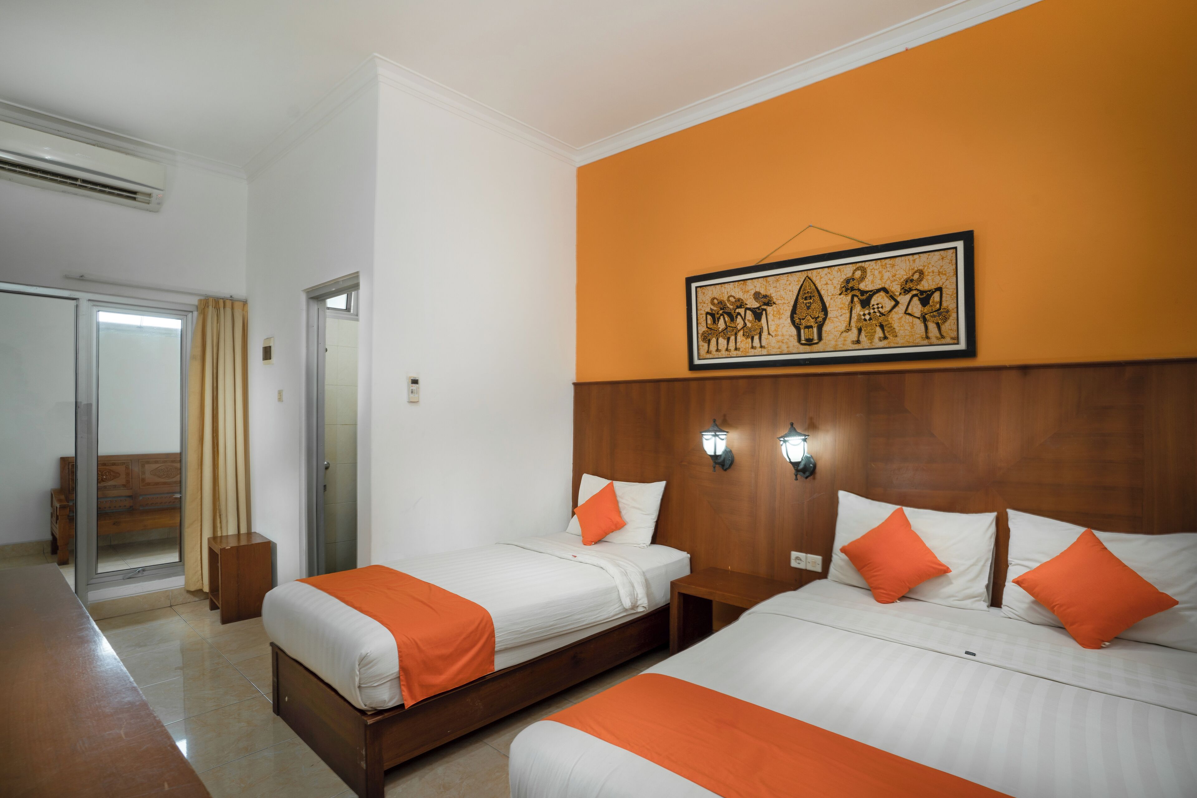 A hotel room with two beds, a wooden headboard, a framed artwork, and a sliding door.
