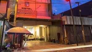 Un hotel con un llamativo letrero de neón, una entrada visible y vista a la calle con vehículos estacionados y una bicicleta.