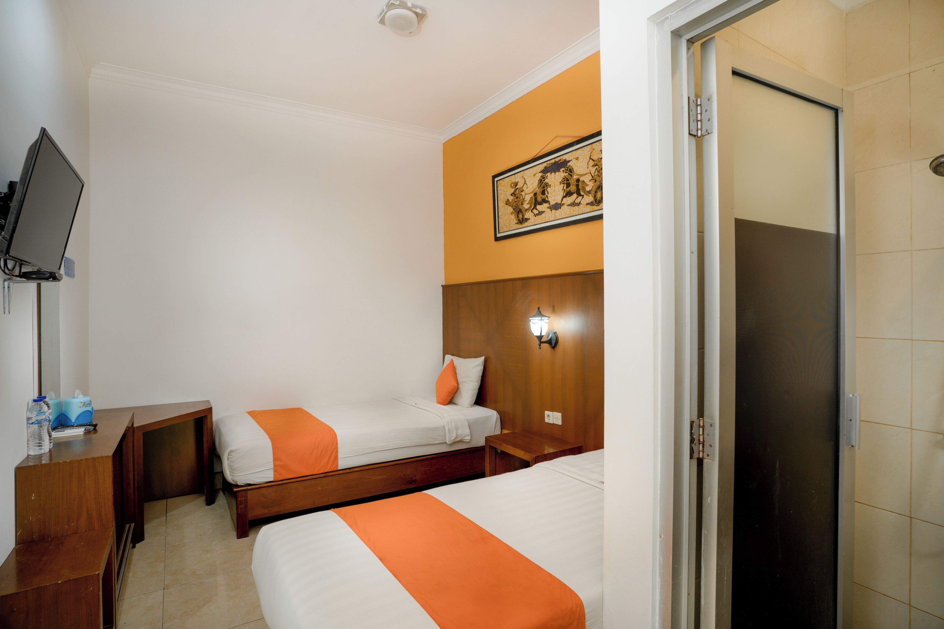 A hotel room with two beds, a desk, a television, and a door.
