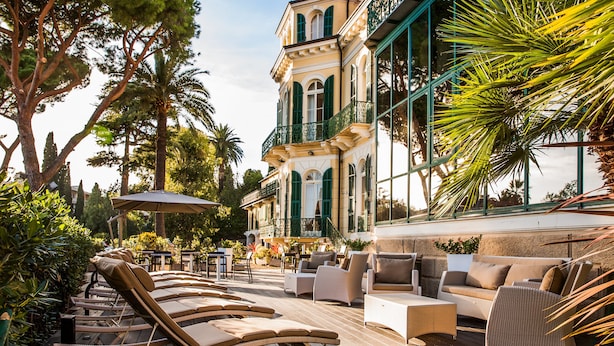 A terrace with sun loungers, outdoor seating, and a building with large windows and balconies. - Villa Sylva & Spa (Sanremo)