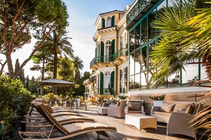 A terrace with sun loungers, outdoor seating, and a building with large windows and balconies. - Villa Sylva & Spa (Sanremo)