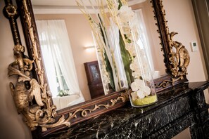 A mirror with ornate gold detailing, a vase with white flowers, and a marble fireplace. - Villa Sylva & Spa (Sanremo)