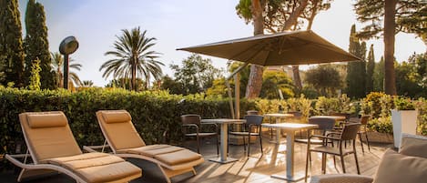 Une terrasse avec des chaises longues, une table et un parasol.