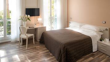 Una habitación de hotel con cama, escritorio con silla, televisor y ventana con cortinas.