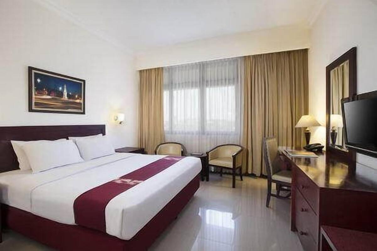 A hotel room with a large bed, a desk with a chair, a television, and a window with curtains.